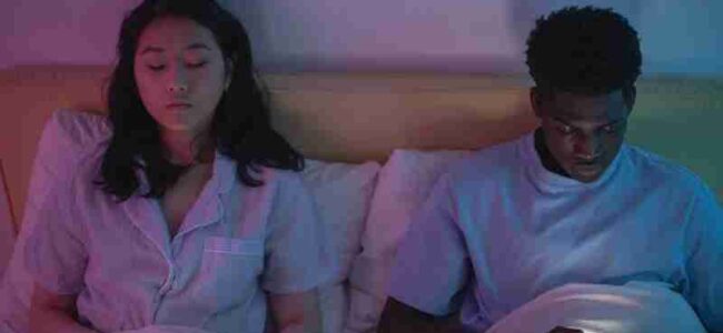 Interracial couple in bed at night using smartphones, illuminated by screen glow, wearing pajamas., tags: die - pexel